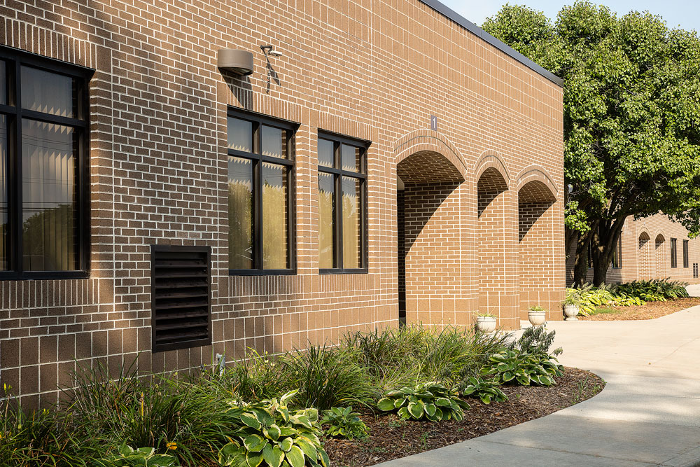Exterior side view of the Lutz school building. Brick face with hostas and daylillies outside.